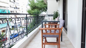 Ein Balkon mit einem Holztisch und Stühlen, einer Topfpflanze und Blick auf die Straße darunter.