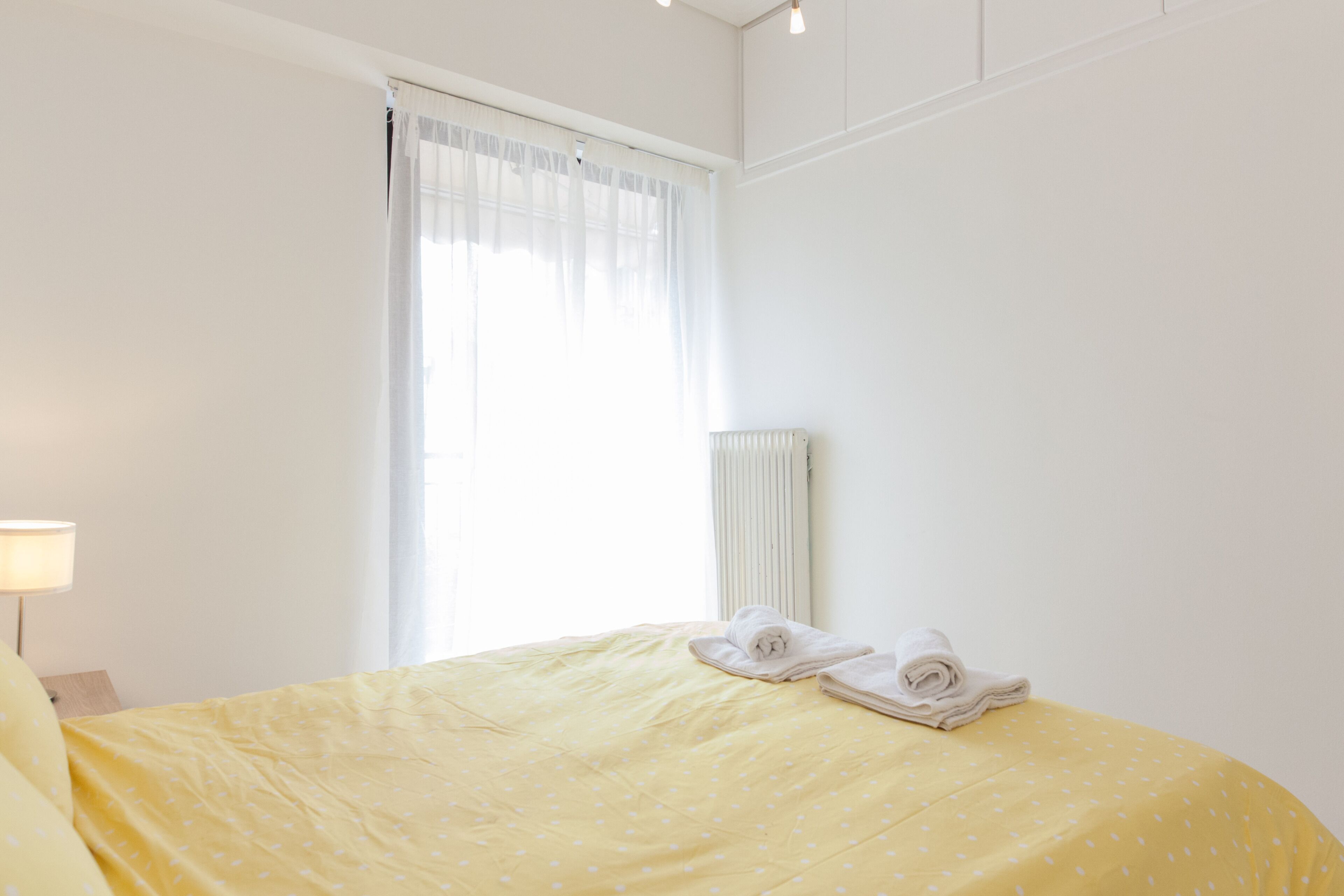 Ein Hotelzimmer mit Bett, Fenster mit durchsichtigen Vorhängen, Heizkörper und Lampe.