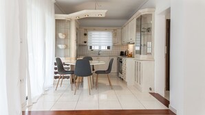 Eine moderne Küche mit weißen Schränken, ein Essbereich mit rundem Tisch und Stühlen sowie eine Treppe zu einer weiteren Ebene.