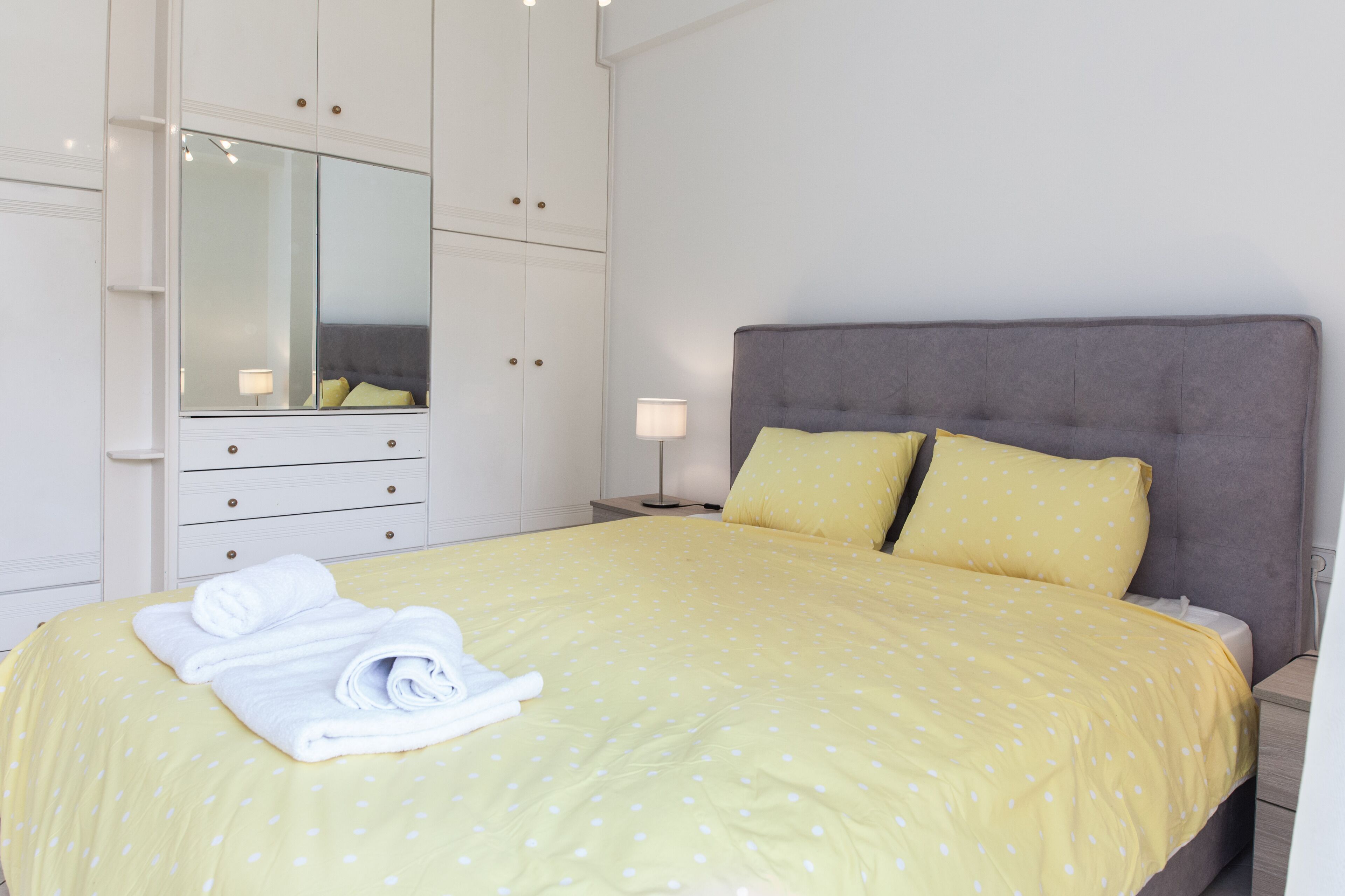 A neatly made bed with a yellow polka dot bedspread, two pillows, and a folded towel on the foot of the bed.