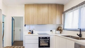A compact kitchen with white cabinetry, a built-in oven, a sink, and a window with a view. - The Sweet Retreat - Hot tub with Lakeviews! (Tuggerawong)