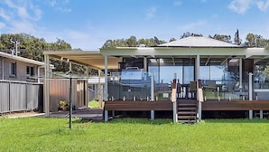 A modern building with a covered outdoor seating area, a fenced yard, and a view of the surrounding landscape. - The Sweet Retreat - Hot tub with Lakeviews! (Tuggerawong)