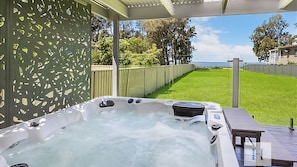 Un jacuzzi con cubierta de madera y vista a un jardín con césped y árboles.