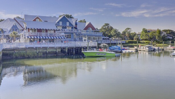 A waterfront building with a dock, a green boat named 'Papasail', and a calm lake. - Sunset Rentals | Bluff Villas 1768 (Hilton Head Island)