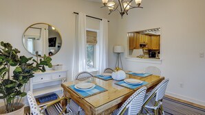 A dining area with a wooden table, white chairs, and a chandelier. - Sunset Rentals | Bluff Villas 1768 (Hilton Head Island)