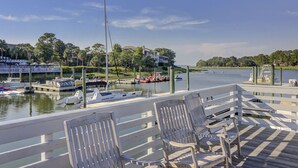 A marina with boats docked, a wooden deck with chairs, and a view of a house across the water. - Sunset Rentals | Bluff Villas 1768 (Hilton Head Island)