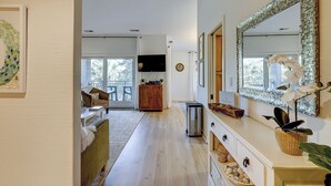 A spacious living room with a large mirror, a sofa, a television, and a view of the outdoors through a sliding door. - Sunset Rentals | Bluff Villas 1768 (Hilton Head Island)