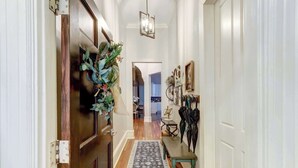 A hallway with a patterned rug, a hanging plant, and a coat rack with bags. - The Alfred Inn, Victorian District | Modern Flare (Savannah)