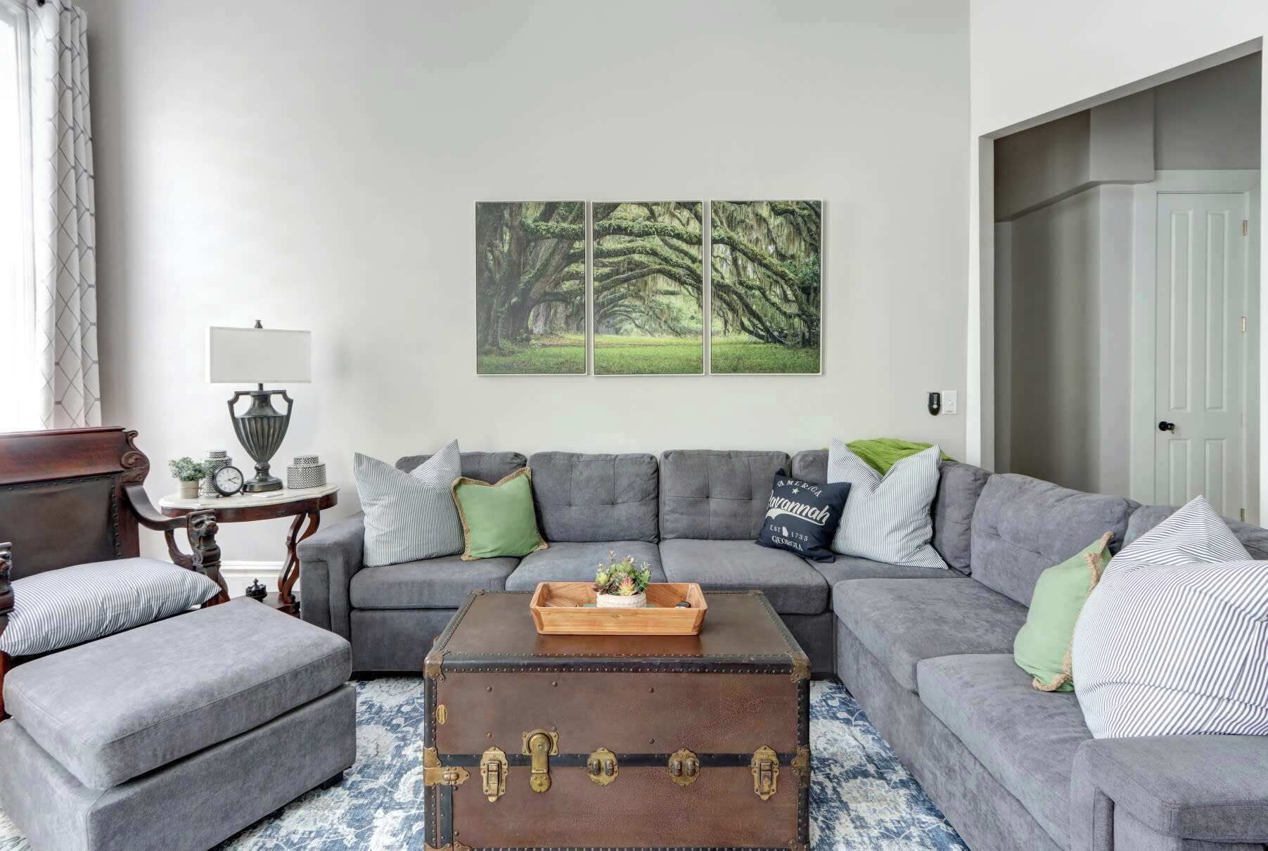 Un salon avec un canapé gris, une table basse en bois et un grand tableau représentant une forêt.