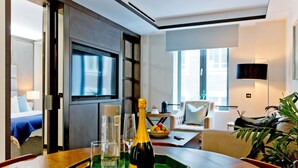 Une chambre d’hôtel avec un coin repas, une télévision, une plante et une bouteille de champagne sur un plateau.