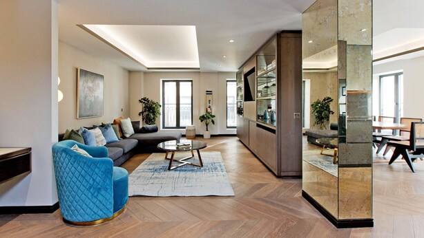 A modern living room with a sofa, a blue armchair, a coffee table, and a large mirror. - 3-bed Deluxe Apt 413 (London)
