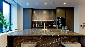 A modern kitchen with a marble island, two bar stools, and a large window. - 3-bed Deluxe Apt 413 (London)