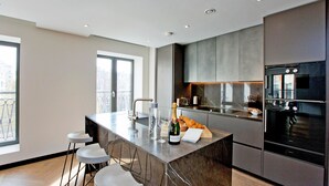 A modern kitchen with a marble island, bar stools, a refrigerator, and a large window. - 3-bed Deluxe Apt 413 (London)