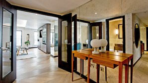 A modern interior with a wooden dining table, a large mirror, and a view into a kitchen and living area. - 3-bed Deluxe Apt 413 (London)