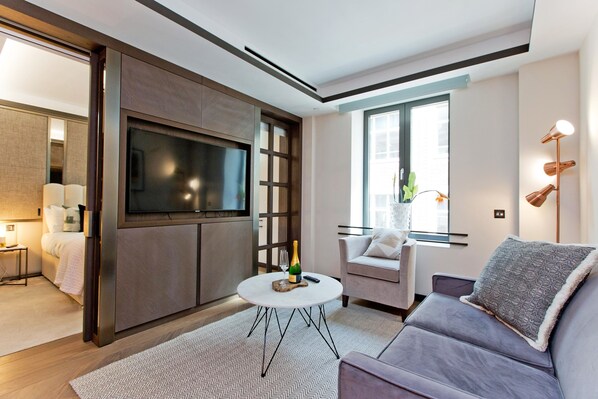 Een moderne woonkamer met een bank, een ronde salontafel, een flatscreen televisie en een raam met uitzicht.