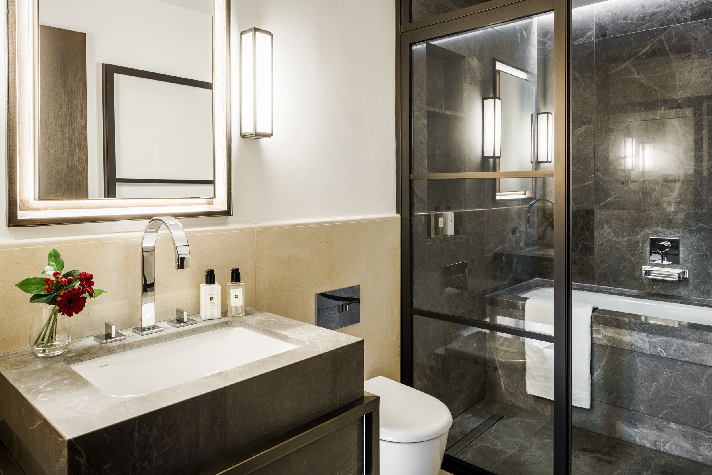 A modern bathroom with a large mirror, a sink, a toilet, and a glass-enclosed shower.