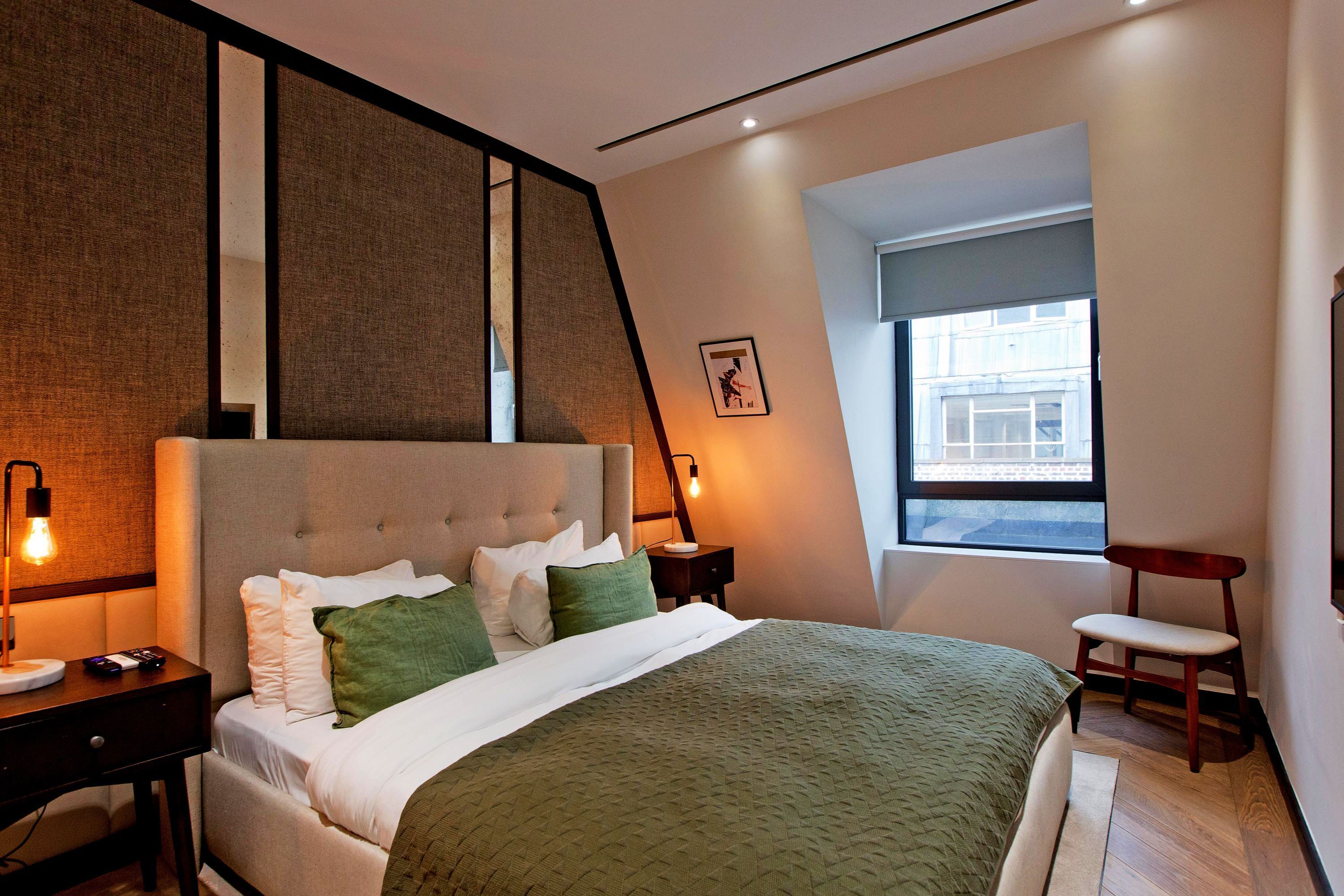 Una camera da letto moderna con un letto, comodini, una sedia, una finestra e un'opera d'arte appesa al muro.