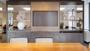 Un comedor moderno con una mesa y sillas de madera, un espejo grande y objetos decorativos en estantes.