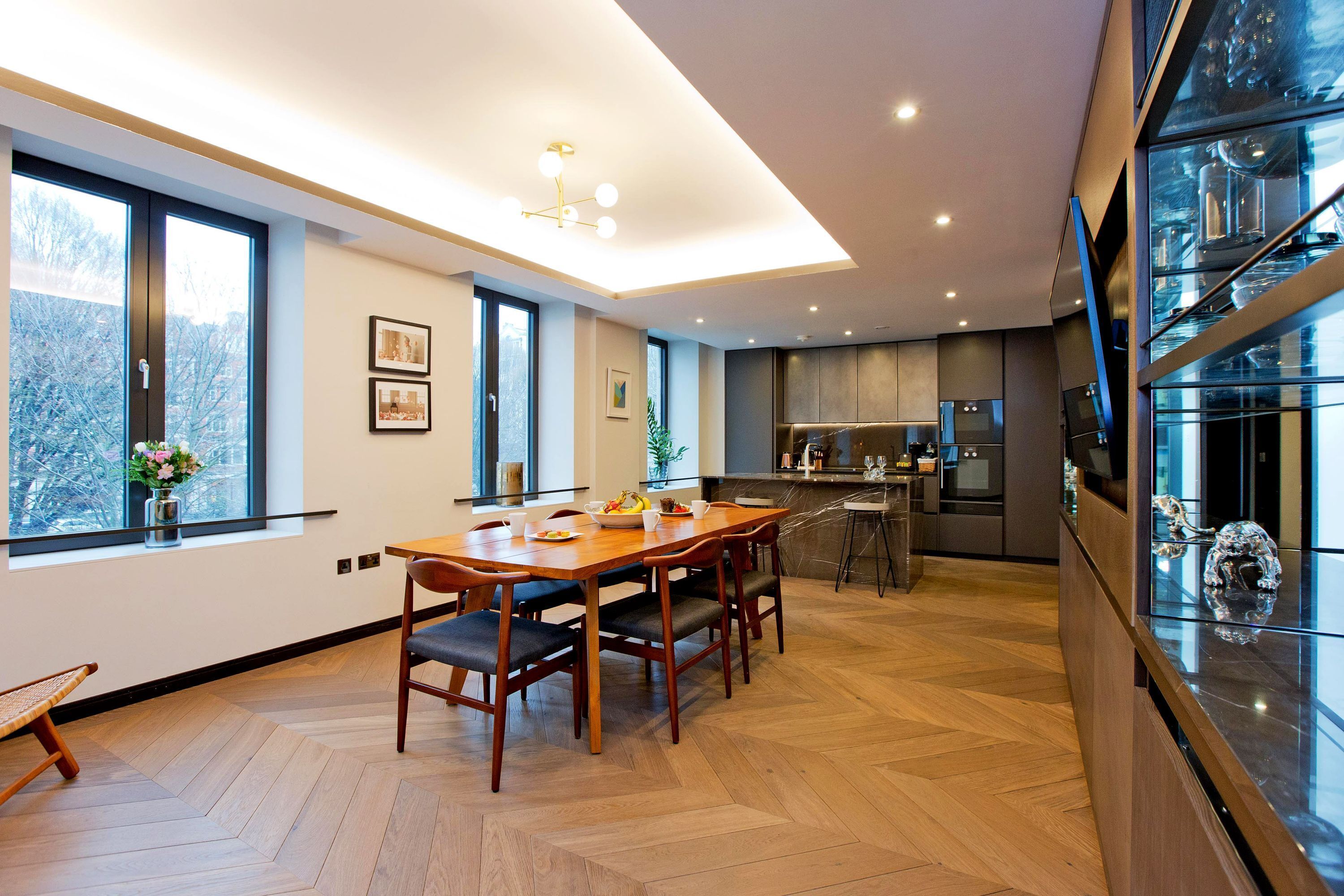 Una cocina moderna con comedor, ventanas amplias y suelo de madera en espiga.