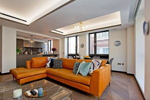 A modern living room with a sectional sofa, a coffee table, and a kitchen area in the background. - 2-bed Superior Apt 208 (London)