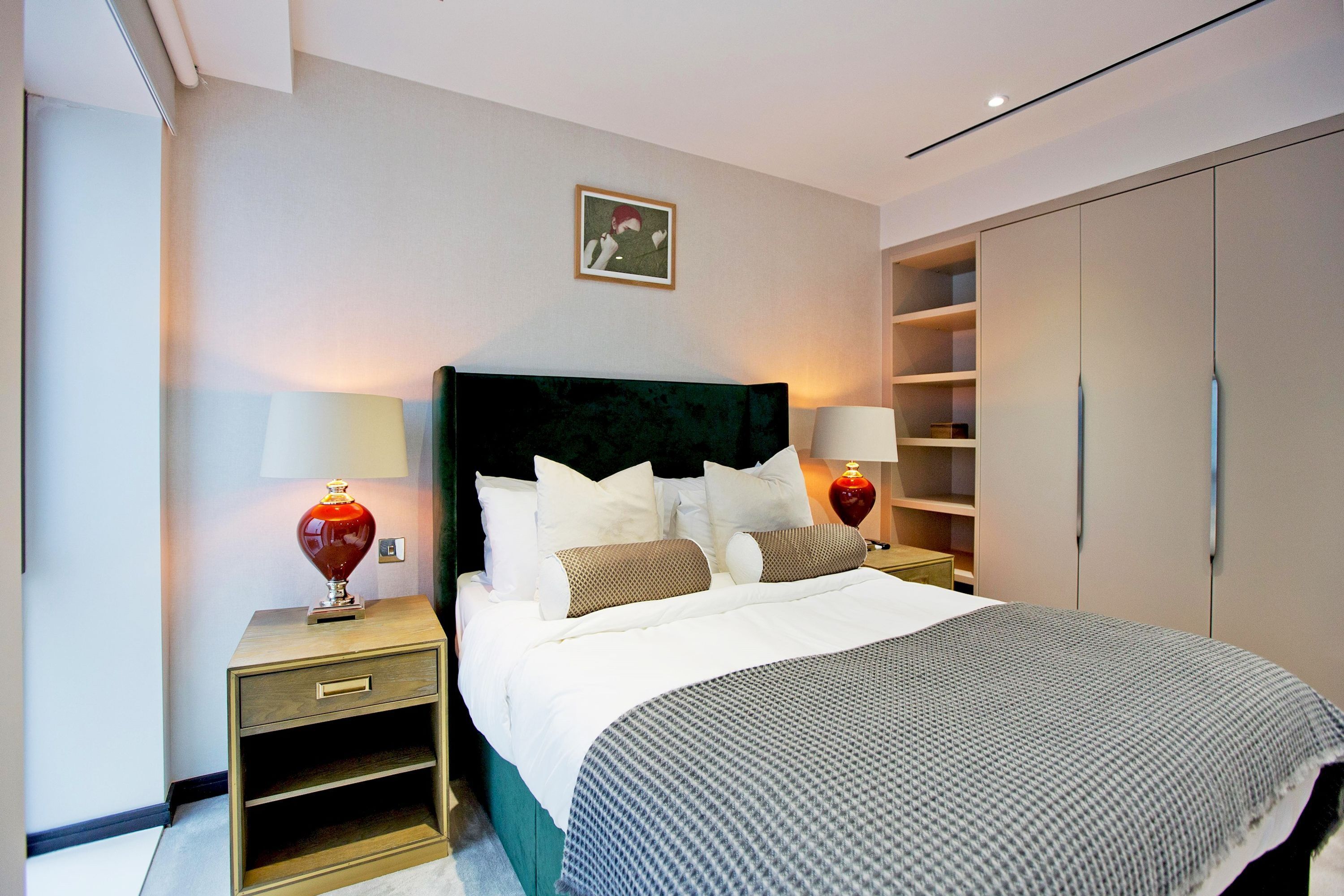 Quarto de hotel bem arrumado, com uma cama, mesas de cabeceira, guarda-roupa e um quadro na parede.