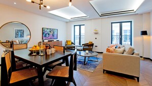 A modern living room with a dining area, large windows, and a ceiling light fixture. - 2-bed Superior Apt 415 (London)