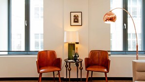 Une pièce comprenant deux fauteuils en cuir, une table avec une bouteille et des verres, une lampe et un tableau encadré au mur.