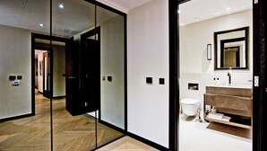 Une chambre d’hôtel moderne dotée d’une paroi en verre, d’un plancher en bois, d’une salle de bain avec un comptoir en marbre et d’un grand miroir.