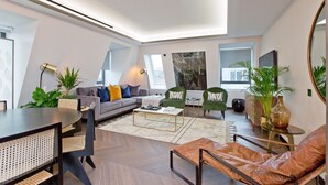 Una sala de estar moderna con un sofá, una mesa de centro y sillas. Hay plantas, un espejo y una ventana.