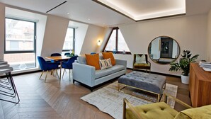 A modern living room with a sofa, ottoman, and dining area. - 2-bed Superior Apt 416 (London)