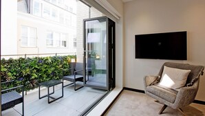 Un salon moderne doté d’une porte vitrée donnant sur un balcon, d’un téléviseur à écran plat fixé au mur et d’un fauteuil confortable.