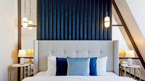 Une chambre d’hôtel avec un grand lit, deux tables de chevet avec des lampes, une tête de lit avec des lattes verticales et un plafond en pente.