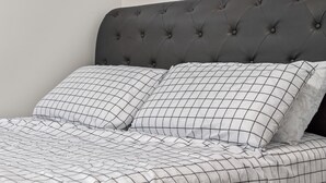 Ein Bett mit einer gepolsterten Kopfteil, zwei Kissen mit Rautenmuster und eine Bettdecke mit ähnlichem Muster.