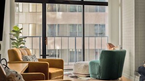 Ein modernes Wohnzimmer mit großem Fenster, einer Couch, einem grünen Sessel und einem kleinen Tisch.