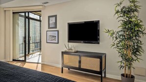 Ein modernes Schlafzimmer mit einem großen Bett, einem Fernseher, einem Rattankorpus und einer Zimmerpflanze.