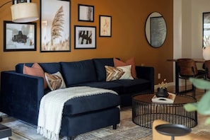 Een moderne woonkamer met een donkerblauwe bank, een ronde salontafel en kunstwerken in lijsten aan de muur.