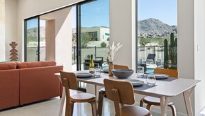 A modern dining area with a table set for four, large windows offering a view of a mountainous landscape, and a cozy seating area with a sofa.