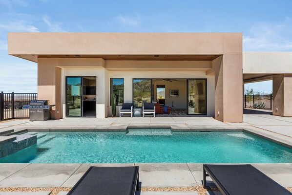 Un área moderna junto a la piscina con vista despejada, una parrilla y una zona de estar con sofá y sillones.