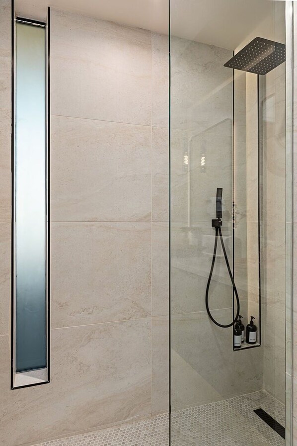 A modern bathroom with a glass-enclosed shower, a large mirror, and a small shelf with toiletries.