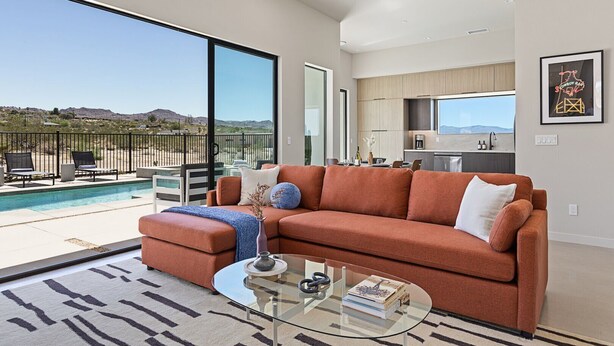 A modern living room with a sectional sofa, a glass coffee table, and a view of a pool and mountains.