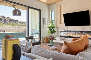 A modern living room with a fireplace, a pool view, and a comfortable seating area. - Crest A at Panorama Villas by Fieldtrip - Luxury 3br retreat w pool (Joshua Tree)