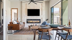 Una sala de estar moderna con chimenea, un sofá, una mesa de comedor para cuatro personas y un ventanal con vistas al exterior.