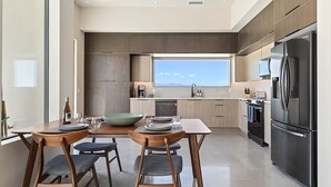 Una cocina moderna con un amplio ventanal, electrodomésticos de acero inoxidable y un comedor con sillas y mesa de madera.