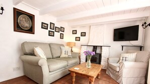 A living room with a sofa, armchair, wooden coffee table, and a fireplace. - Ginentonic Cottage (Helston)