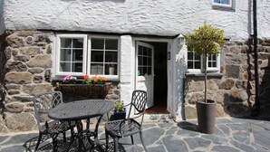 A stone building with white walls and a door leading to a patio area. - Ginentonic Cottage (Helston)