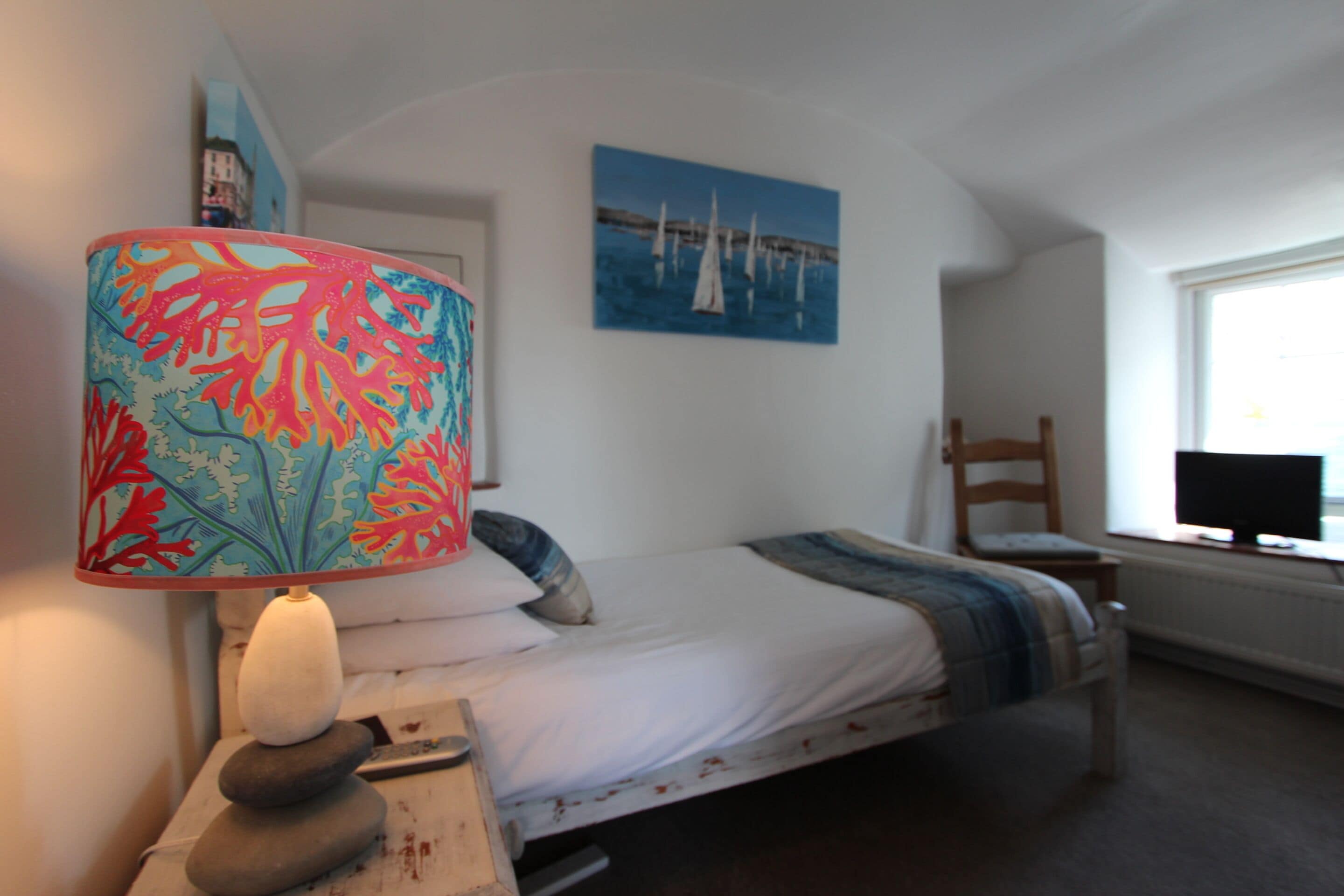 A bedroom with a bed, a lamp, a painting, a chair, and a TV.