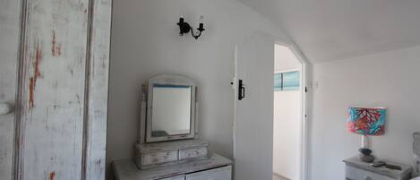 A bedroom with a white dresser, a mirror, a lamp, and a door leading to another room.