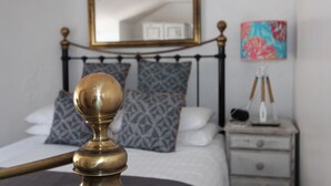 A bed with a brass headboard, a bedside table with a lamp, and a nightstand with a decorative item. - Ginentonic Cottage (Helston)