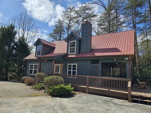 A two-story house with a red roof, a chimney, and a wooden deck.