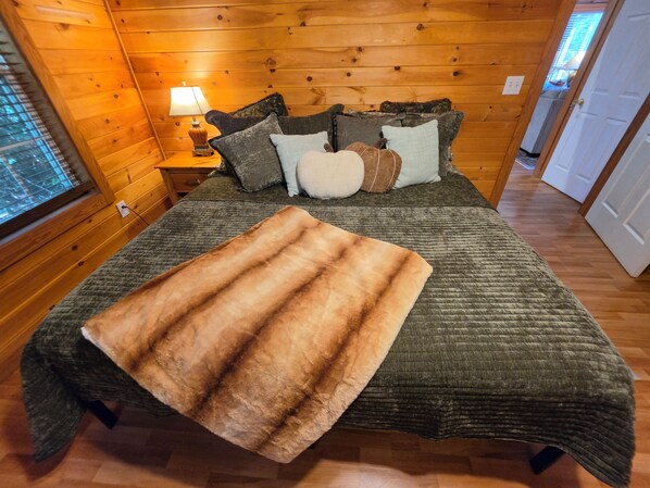 A wooden-paneled bedroom with a bed, pillows, a lamp, and a fur throw.